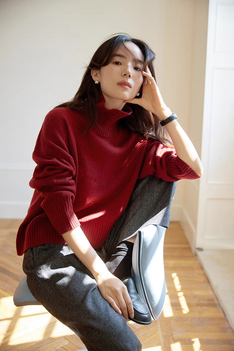 Model in red wool-cashmere turtleneck sweater seated in natural light with relaxed pose highlighting soft drape and cozy feel