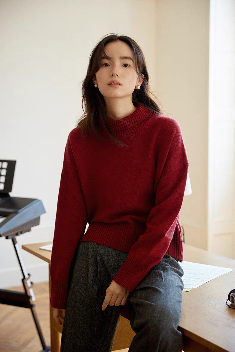 Model wearing red Bordeaux Wool-Cashmere Turtleneck Sweater sitting on desk showcasing relaxed fit, ribbed hem, and soft knit texture
