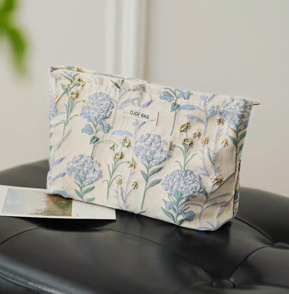 Botanical Embroidered Zip Makeup Pouch in blue floral embroidery placed on sofa with botanical pattern detail