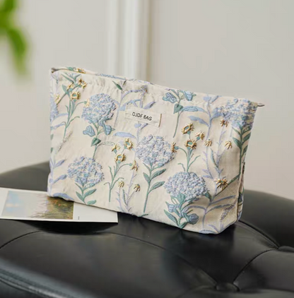 Botanical Embroidered Zip Makeup Pouch in blue floral embroidery placed on sofa with botanical pattern detail