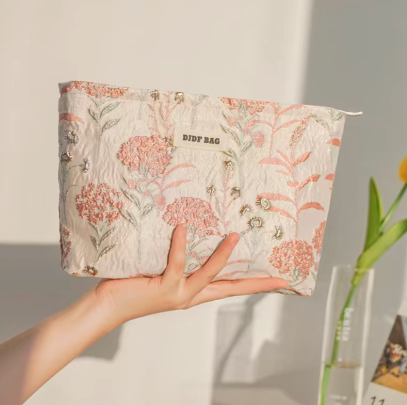 Botanical Embroidered Zip Makeup Pouch in pink floral embroidery held in hand under soft lighting