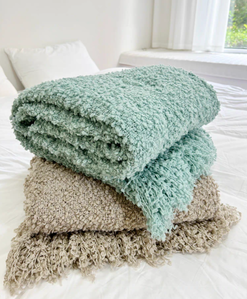 Blue and gray loop knit throw blankets stacked and folded on bed showing tassel fringe detail