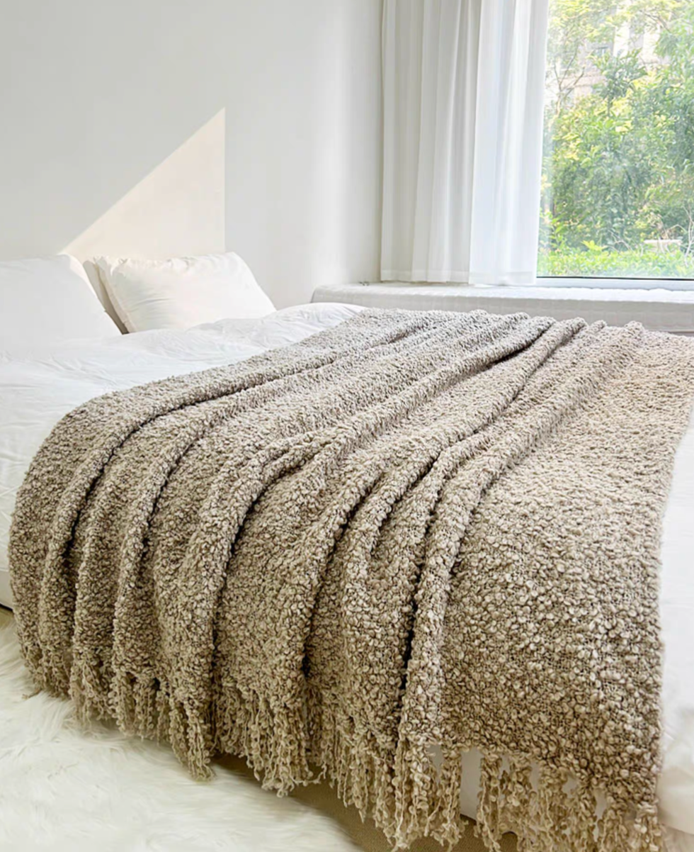 Gray textured loop knit throw blanket with tassel fringe spread across bed showing soft texture