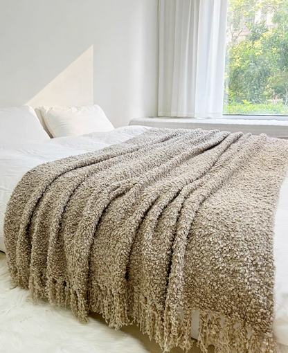 Gray textured loop knit throw blanket with tassel fringe spread across bed showing soft texture