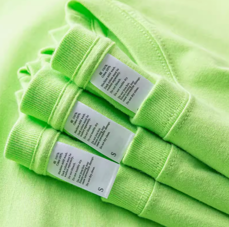 Close-up of green cotton T-shirt care labels showing fabric and size information