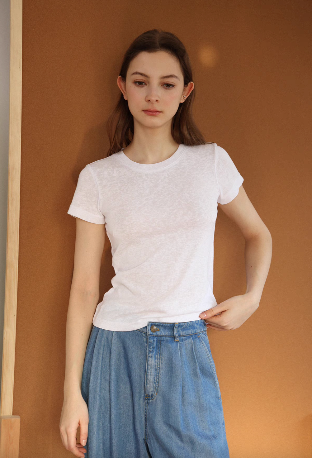 Model wearing Breeze Sheer Classic Tee in white standing against warm wall showing relaxed fit short sleeves and lightweight slub texture