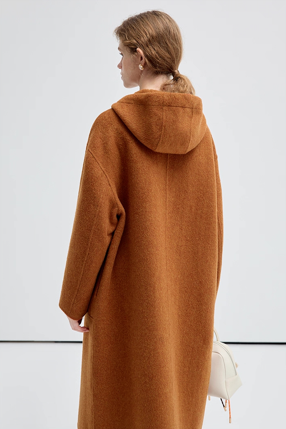 Back view of the model wearing a brown hooded coat, hood naturally draped.