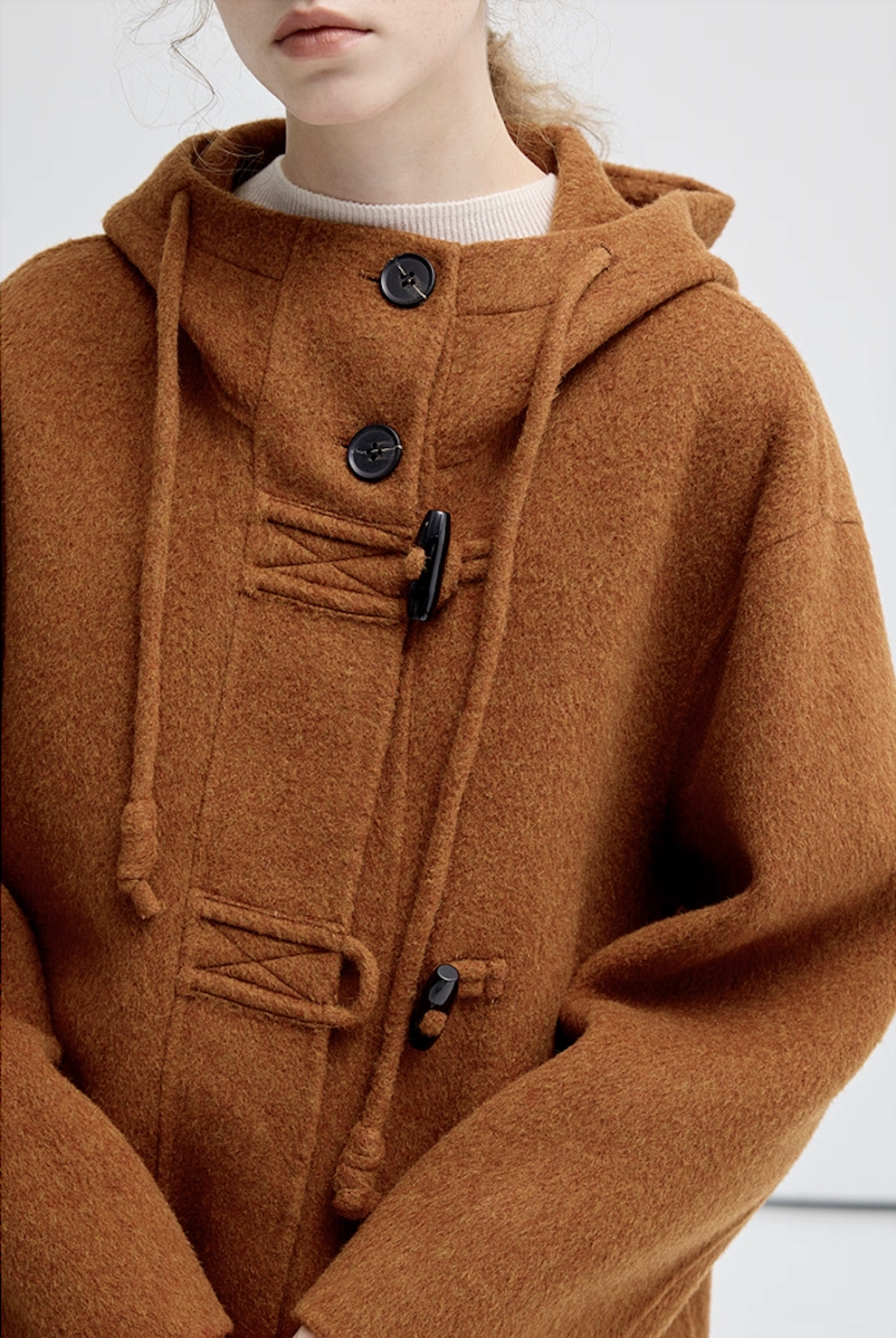 Close-up of the brown hooded coat front, showing buttons, toggles, and drawstring design.