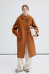 Model wearing a brown hooded wool coat, holding a white handbag, full front view.
