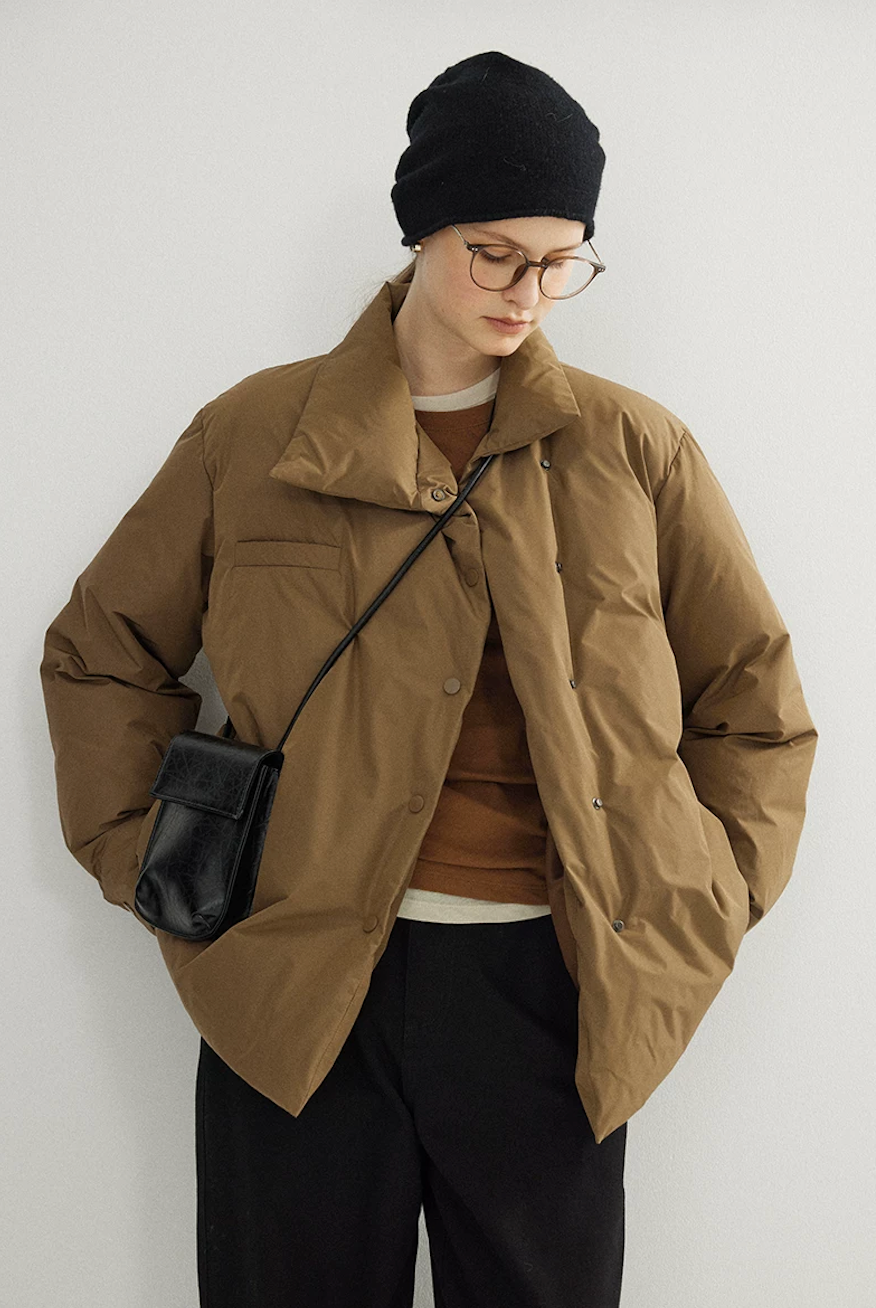 Camel down jacket with the collar turned up, worn partly open with hands in the side pockets