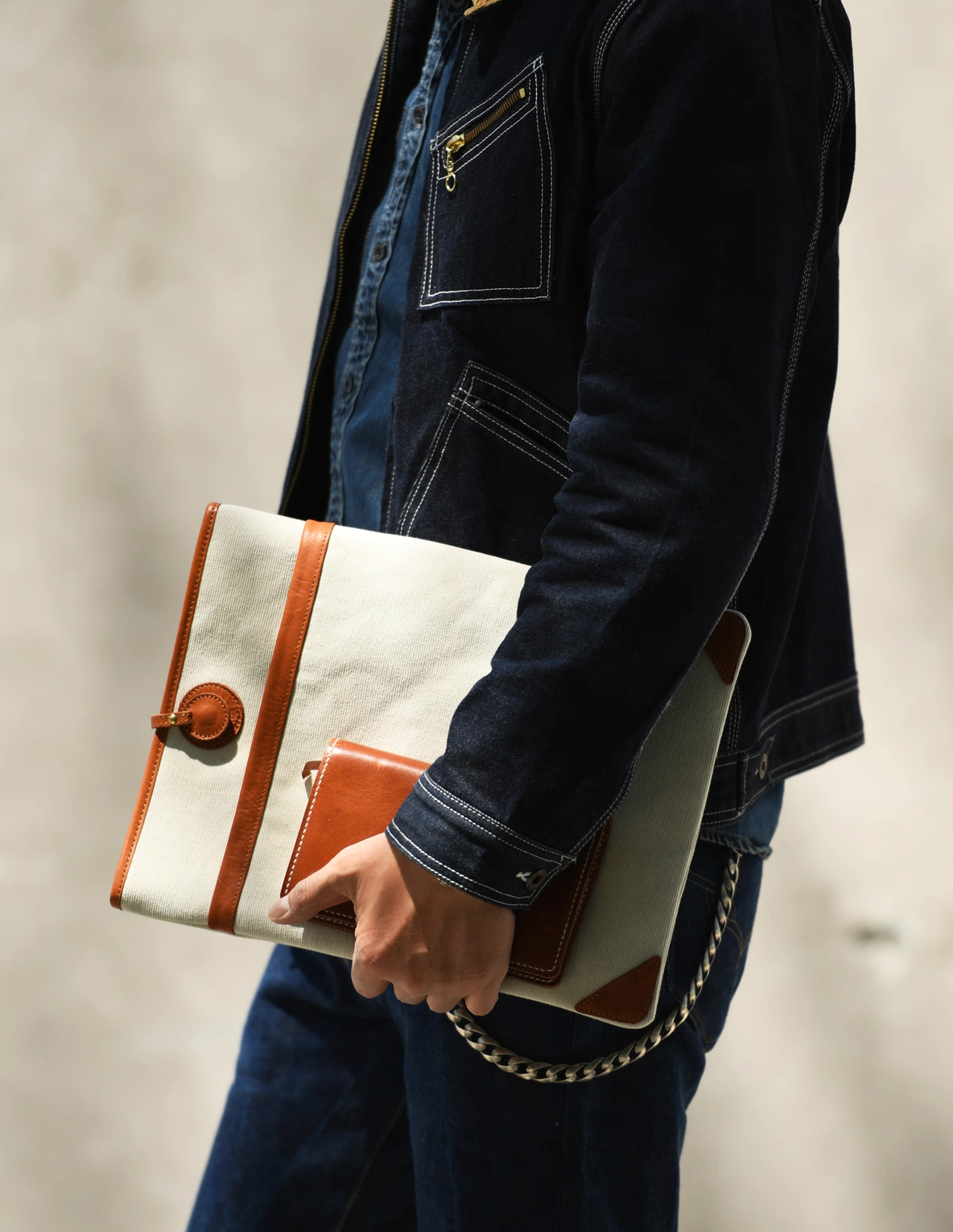 Side view of person carrying an ivory canvas and leather laptop sleeve under the arm in a denim outfit.