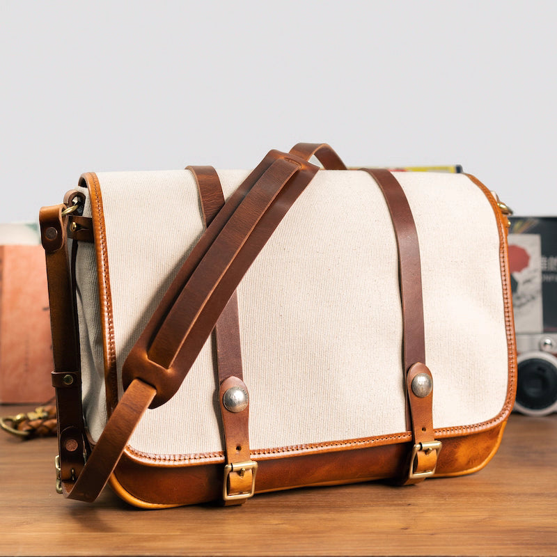 Angled view of beige canvas messenger bag showing leather shoulder strap and trim