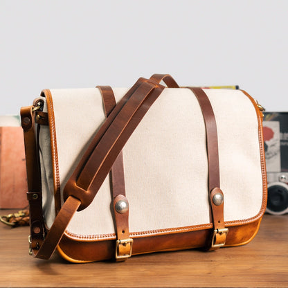 Angled view of beige canvas messenger bag showing leather shoulder strap and trim