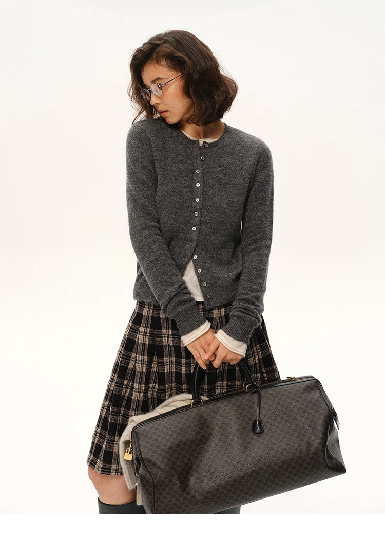Woman wearing charcoal gray alpaca cardigan holding dark patterned travel bag