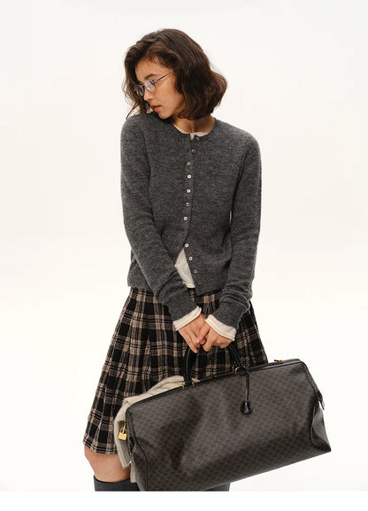 Woman wearing charcoal gray alpaca cardigan holding dark patterned travel bag