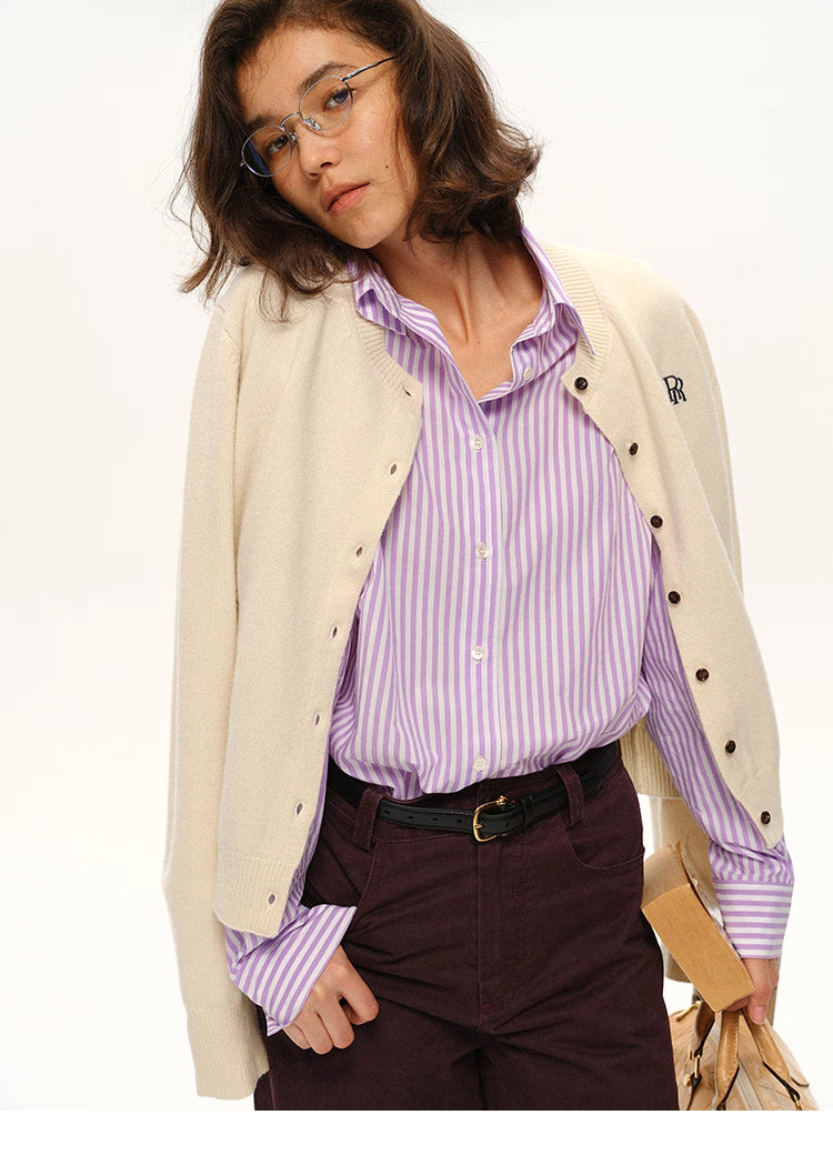 Close-up of cream wool cardigan layered over lilac striped shirt with relaxed modern styling
