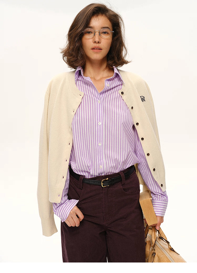Model wearing cream wool cardigan draped over shoulders with lilac striped shirt and burgundy pants
