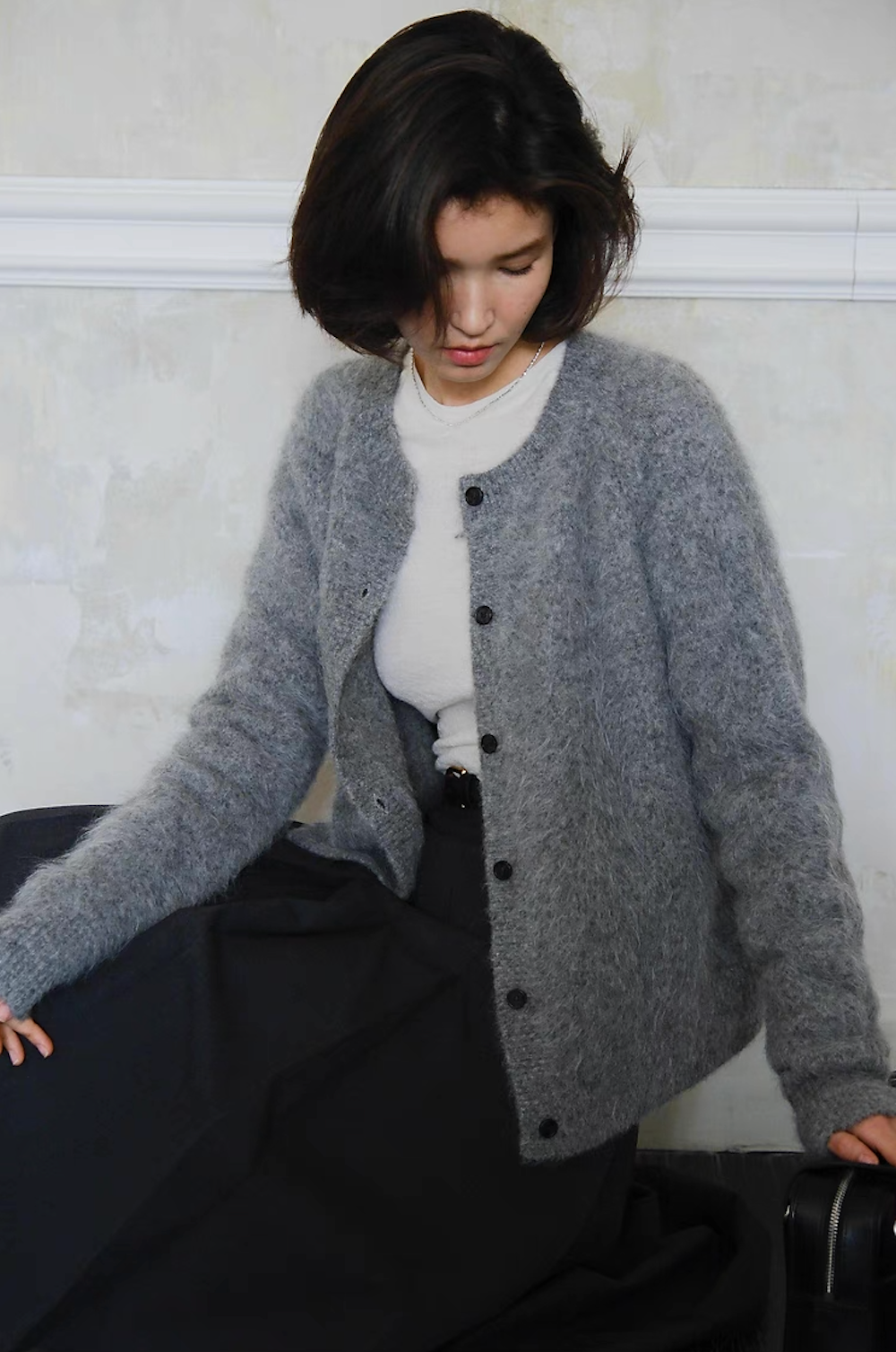 Woman in cozy grey cardigan seated with soft winter knitwear look