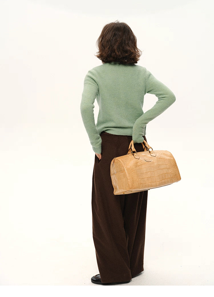 Back view of woman wearing mint green alpaca cardigan holding beige duffle bag
