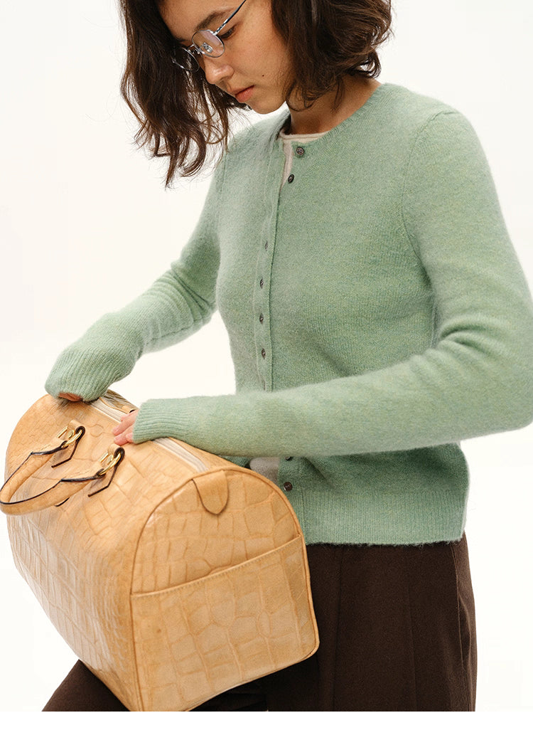 Close view of mint green alpaca cardigan as model handles beige textured duffle bag