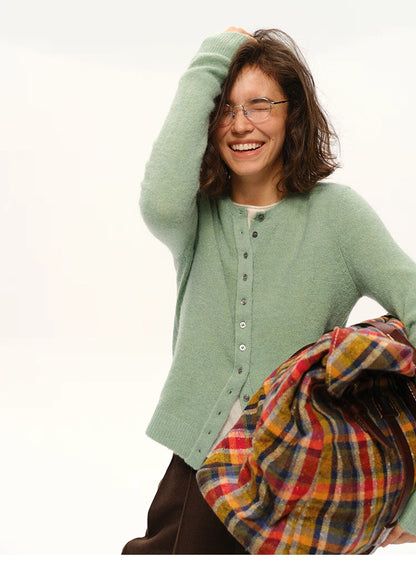 Woman smiling in mint green alpaca cardigan holding colorful plaid blanket bag