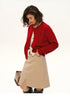 Model wearing cherry red wool logo cardigan styled with beige skirt, hands in pockets, front profile view