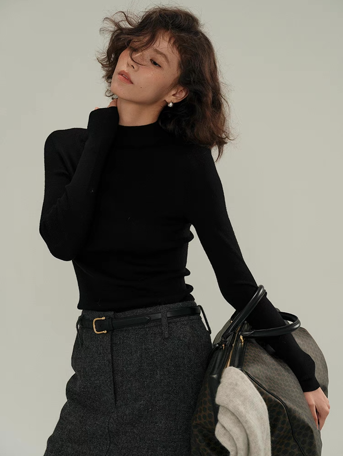 Woman in black fitted cashmere sweater posing with bag – modern winter fashion look.