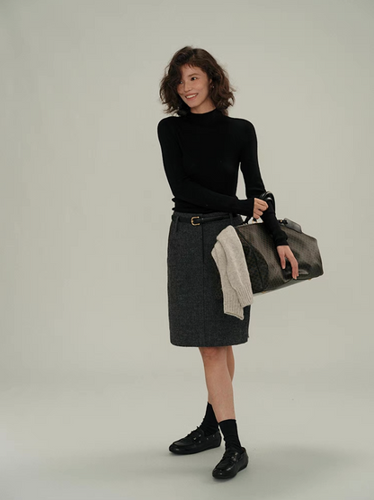 Woman in black cashmere sweater and grey wool skirt smiling, holding travel bag – casual elegant style.