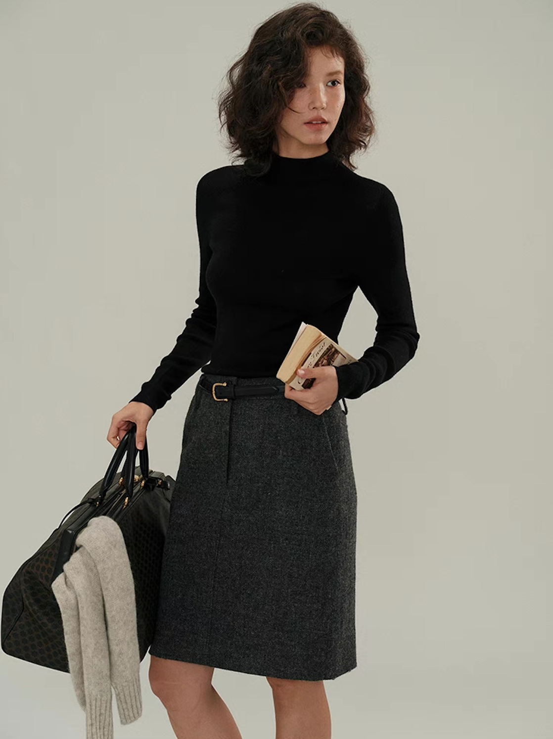 Woman in fitted black cashmere sweater styled with grey skirt and leather belt – classic minimalist outfit.