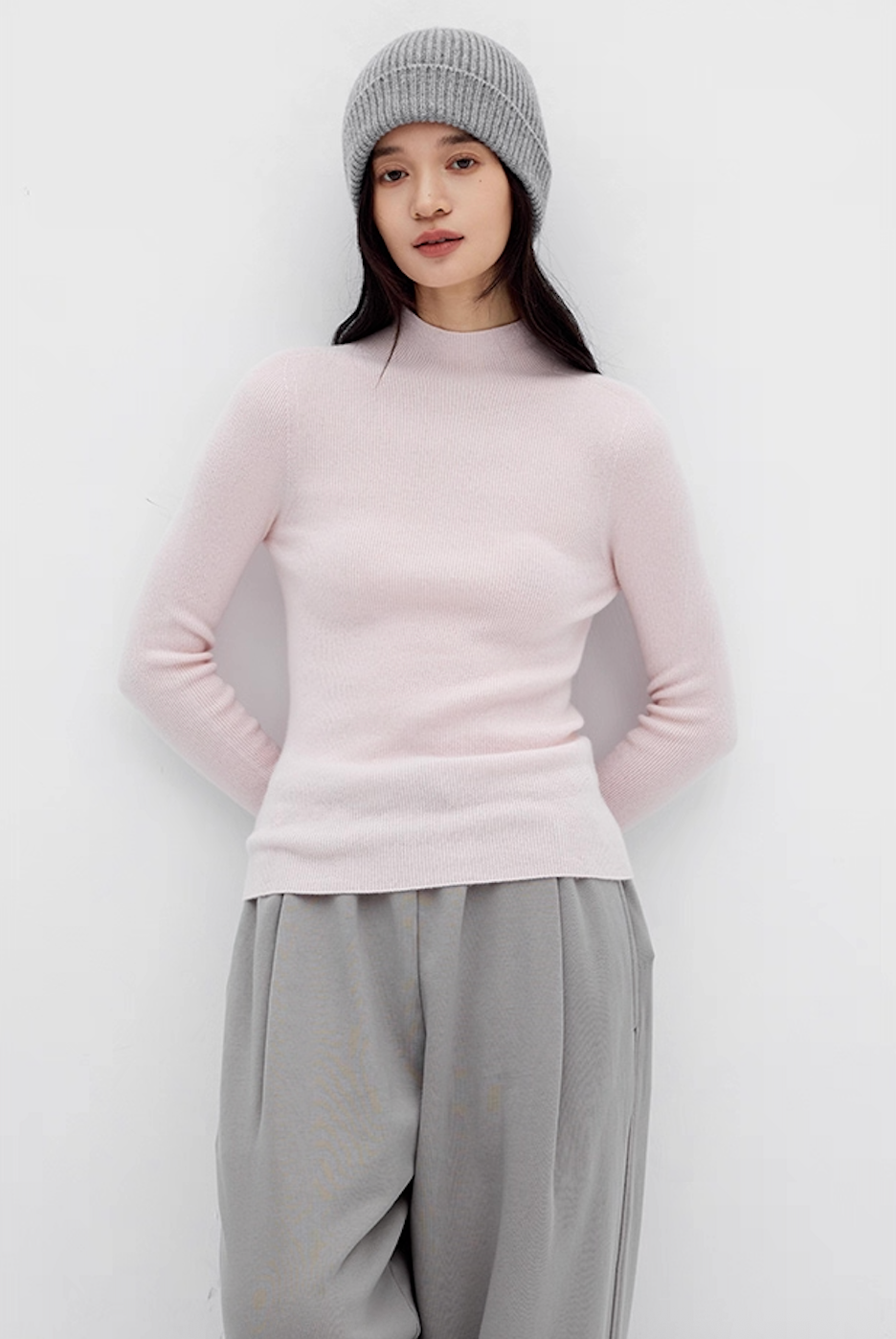 Woman in soft pink slim-fit cashmere sweater with grey wide-leg pants and grey beanie – cozy winter outfit.