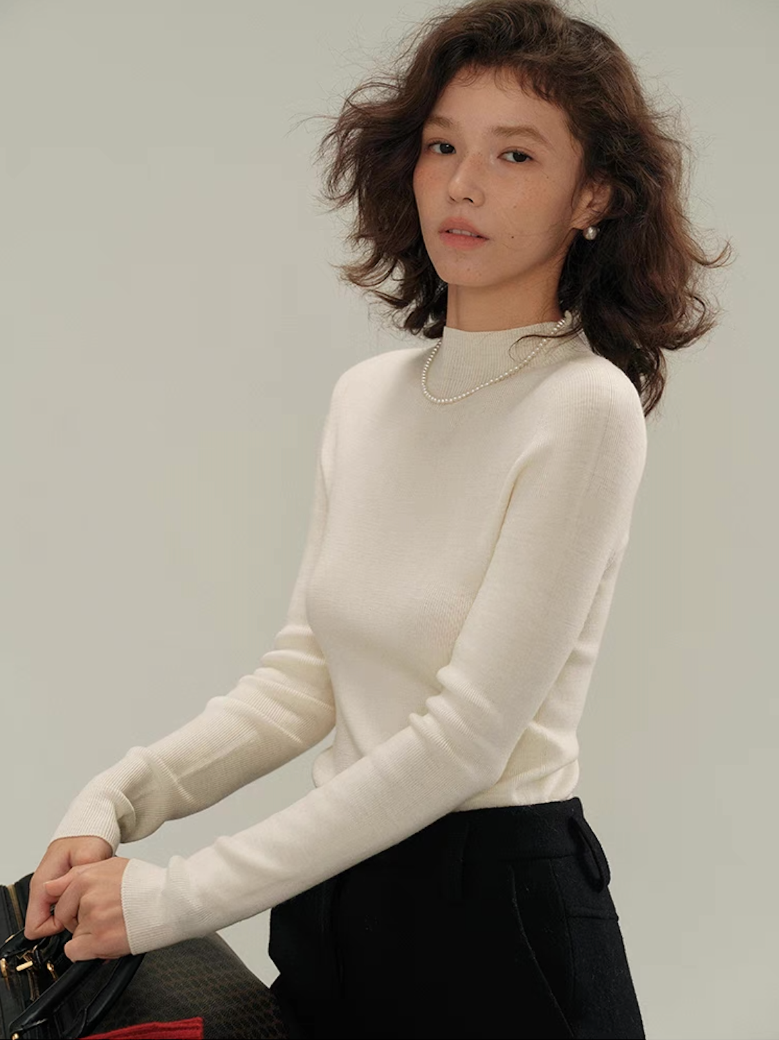 Woman wearing an ivory white cashmere knit sweater with pearl necklace, styled with black skirt – minimalist winter outfit.