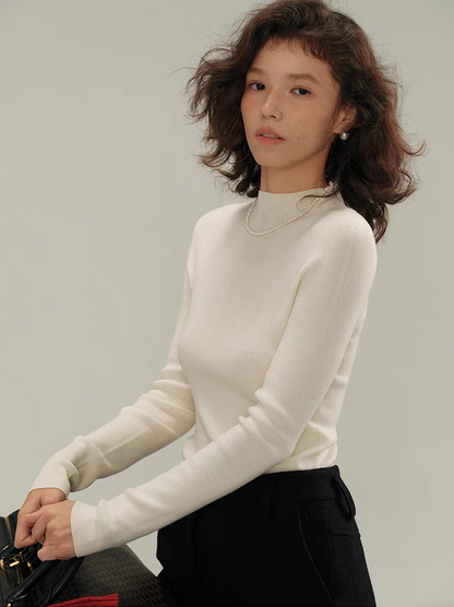Woman wearing an ivory white cashmere knit sweater with pearl necklace, styled with black skirt – minimalist winter outfit.