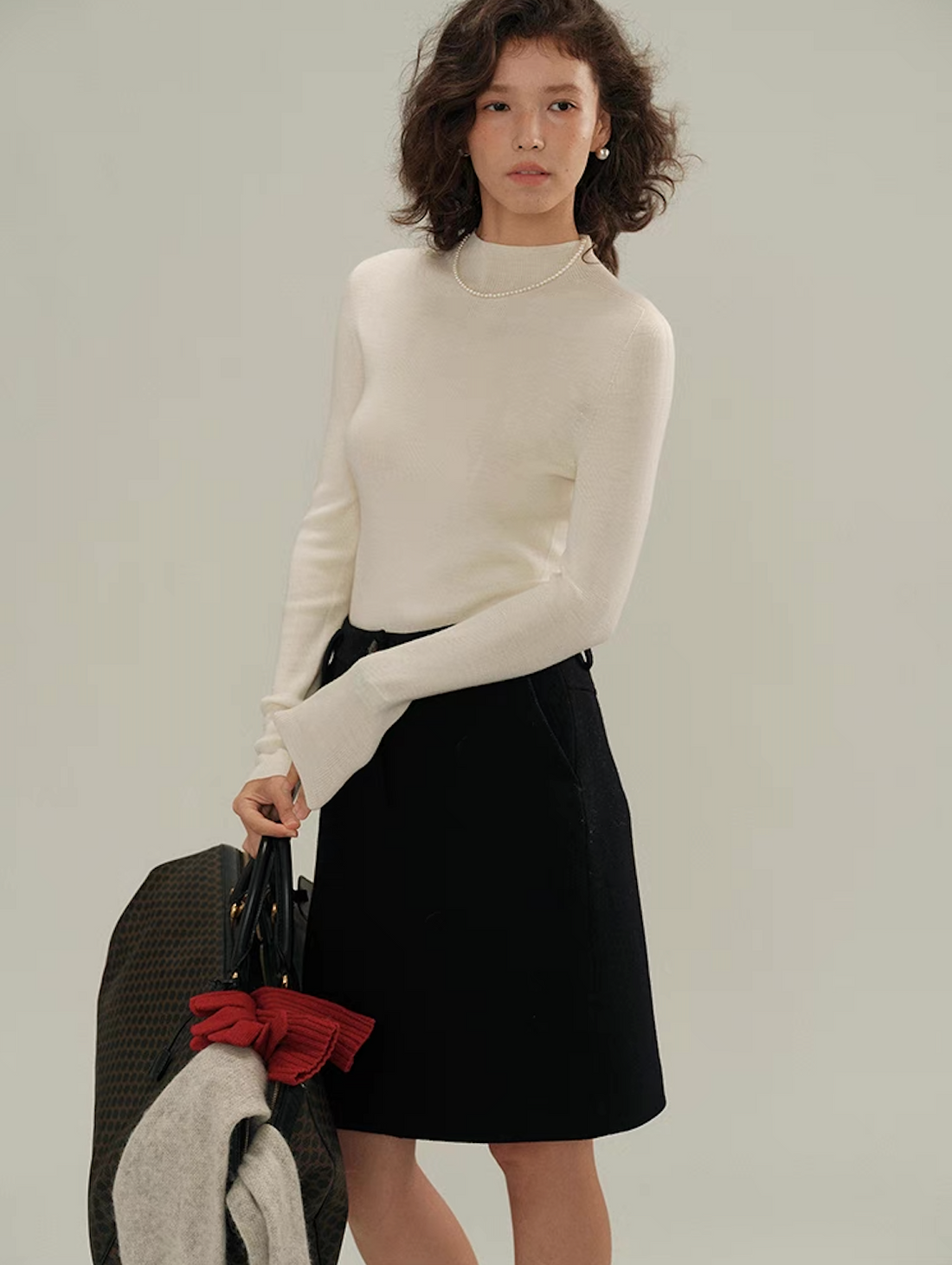 Woman posing in ivory white cashmere sweater with pearl necklace and black skirt – classy knitwear styling.