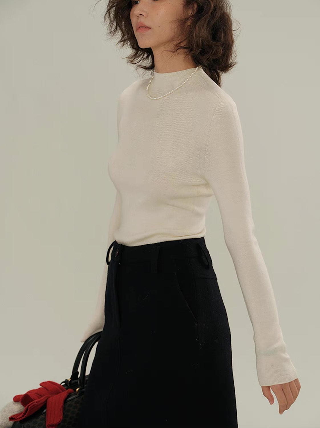 Side view of woman wearing ivory white slim-fit cashmere sweater with black skirt – elegant silhouette.