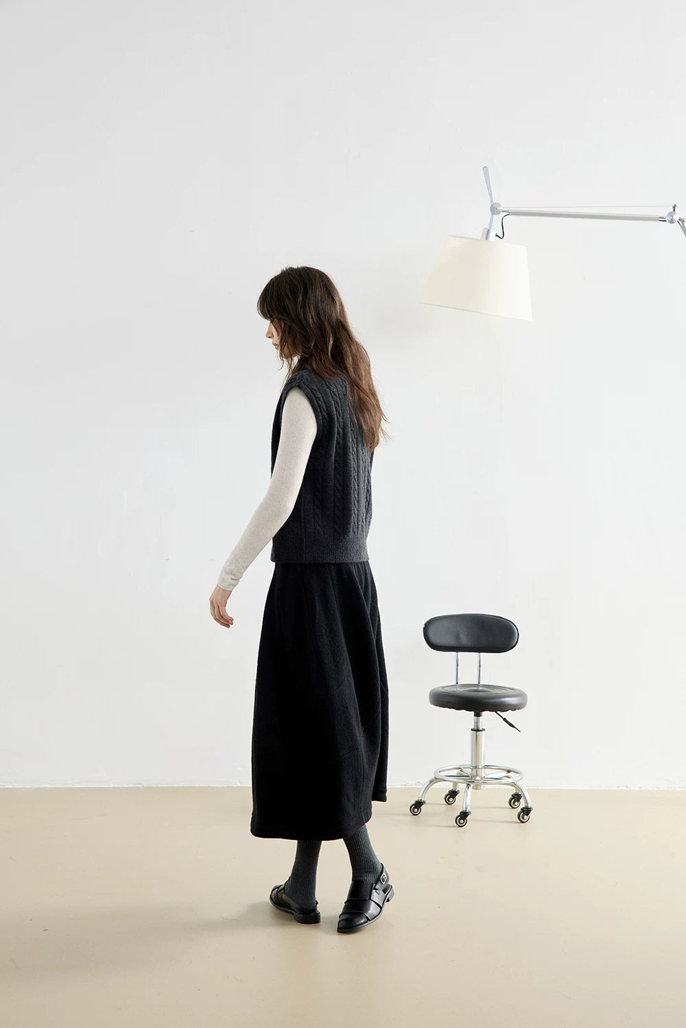 Side view of model walking in Charcoal Gray cable knit vest and black midi skirt