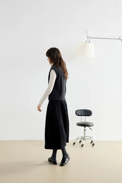 Side view of model walking in Charcoal Gray cable knit vest and black midi skirt