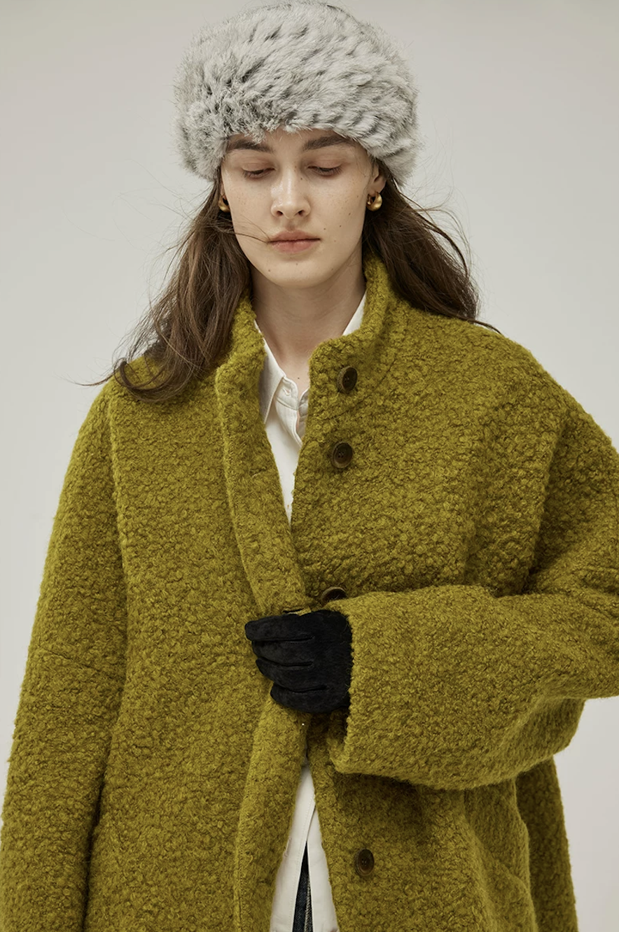 Close-up of a Chartreuse bouclé wool coat with stand collar, tonal brown buttons, and wide sleeve