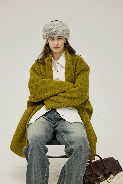 Seated view of a Chartreuse oversized bouclé coat draped loosely with wide dropped sleeves
