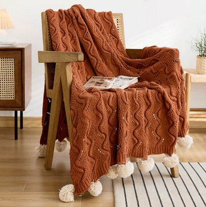 Burgundy chenille throw blanket draped over wooden chair with knitted texture and pom pom tassels