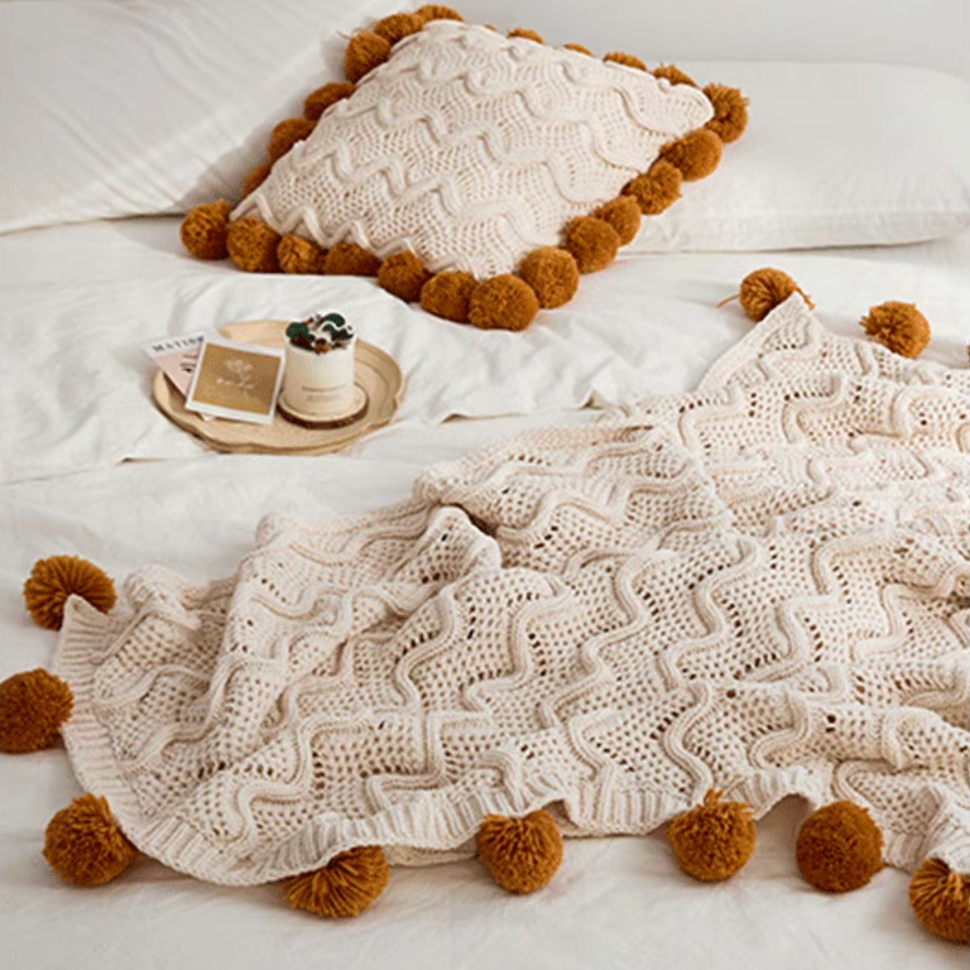 White chenille throw blanket with matching pillow featuring pom pom trim styled on soft bed setting