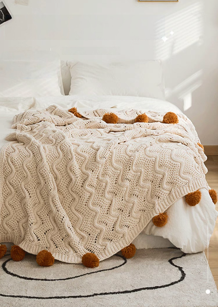 White chenille throw blanket spread across bed in bright bedroom with textured knit and pom pom edges