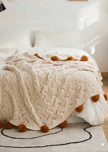 White chenille throw blanket spread across bed in bright bedroom with textured knit and pom pom edges