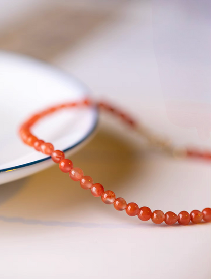 Cherry red agate bead bracelet close-up showing glossy round stones on plate edge