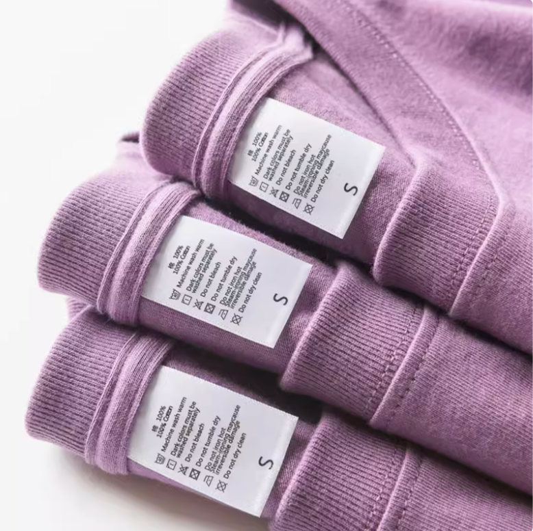 Chic Pocket Tee purple stacked t-shirts with visible care labels showing cotton fabric and stitching detail