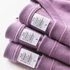 Chic Pocket Tee purple stacked t-shirts with visible care labels showing cotton fabric and stitching detail