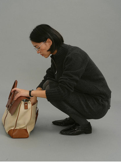 Woman crouching while wearing charcoal wool zip-up cardigan and holding a canvas leather bag