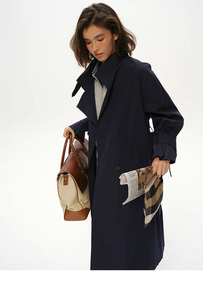 Deep navy trench styled with tote bag and folded newspaper for commuter look.