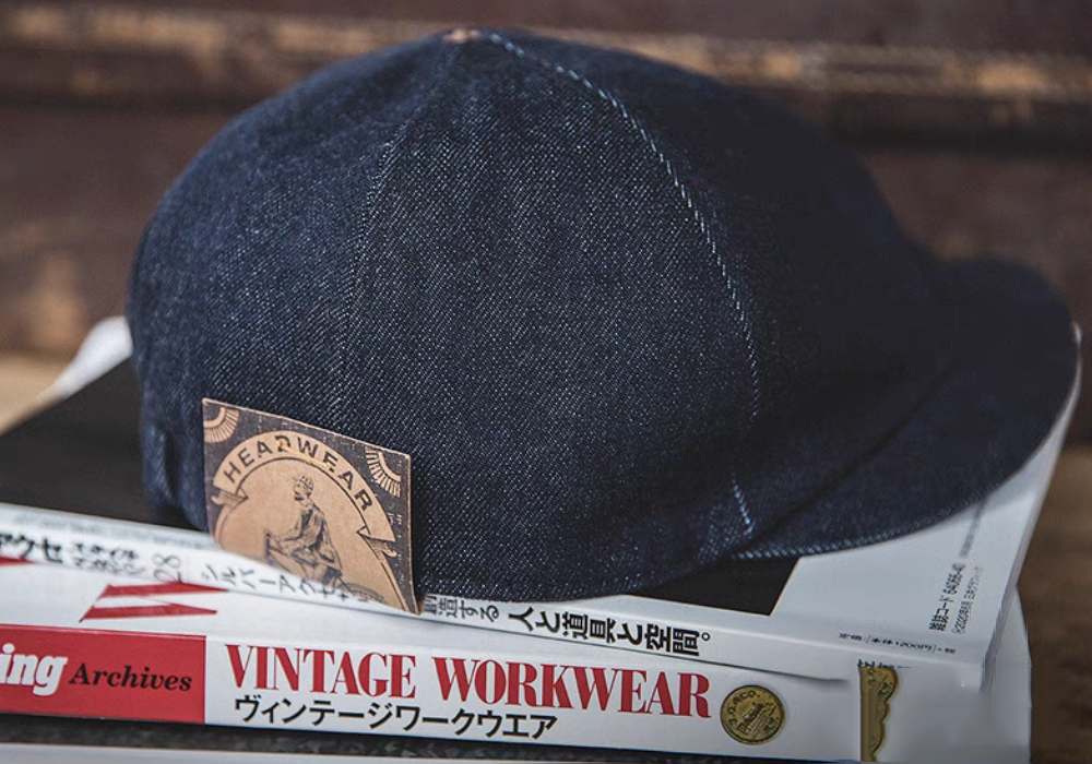 Dark Blue Classic Denim Miki Cap placed on vintage workwear book showing rugged denim texture and heritage inspired styling