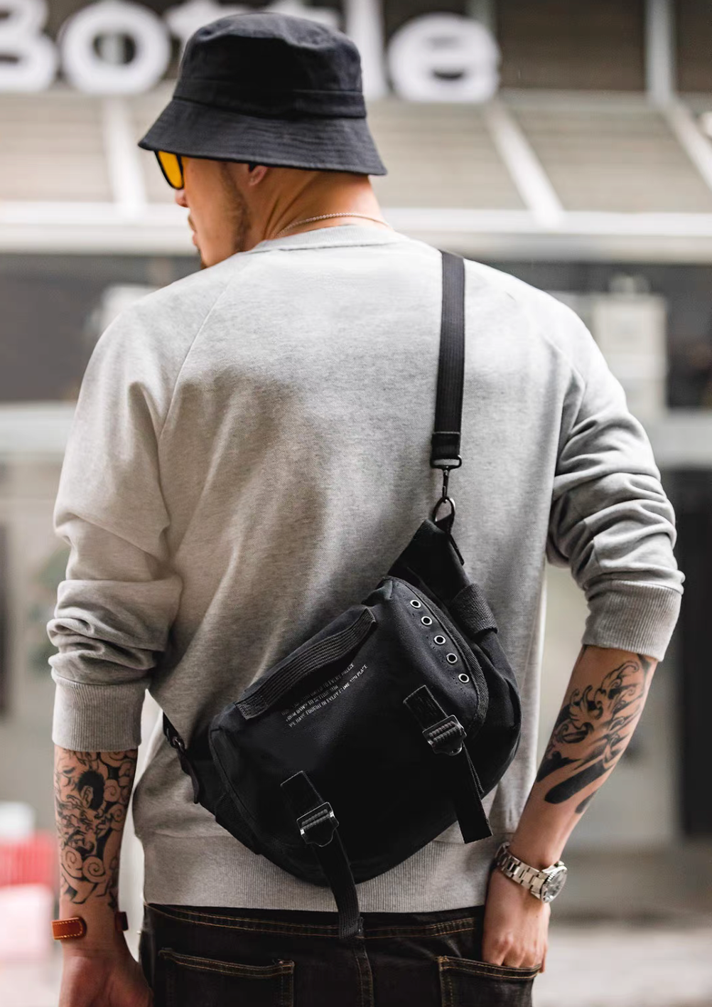 Man wearing black Classic M1961 canvas motorcycle bag crossbody on back showing adjustable strap and urban street style