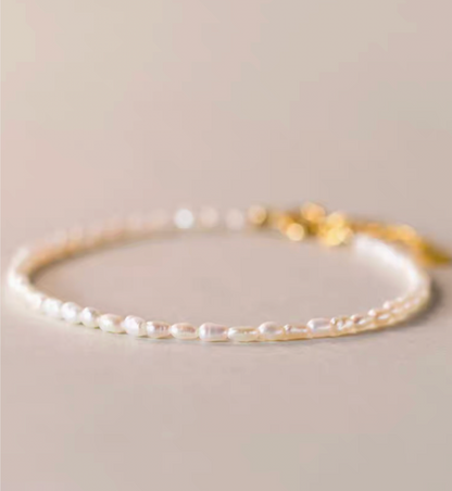 Minimal flat lay close-up showing classic pearl bracelet in natural color with delicate small pearls and gold clasp detail